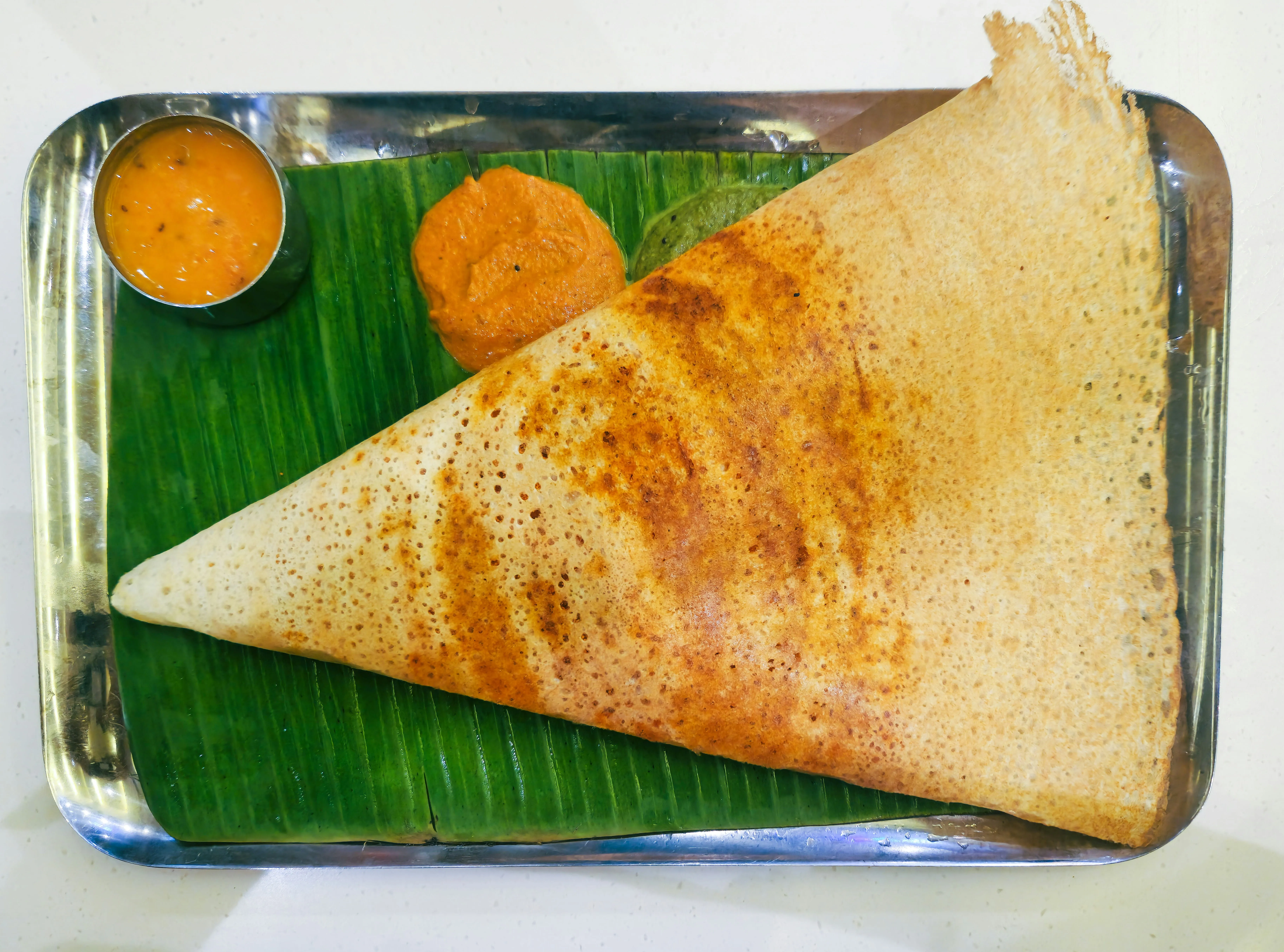 A crispy plain dosa on a metal plate with coconut chutney and sambar
