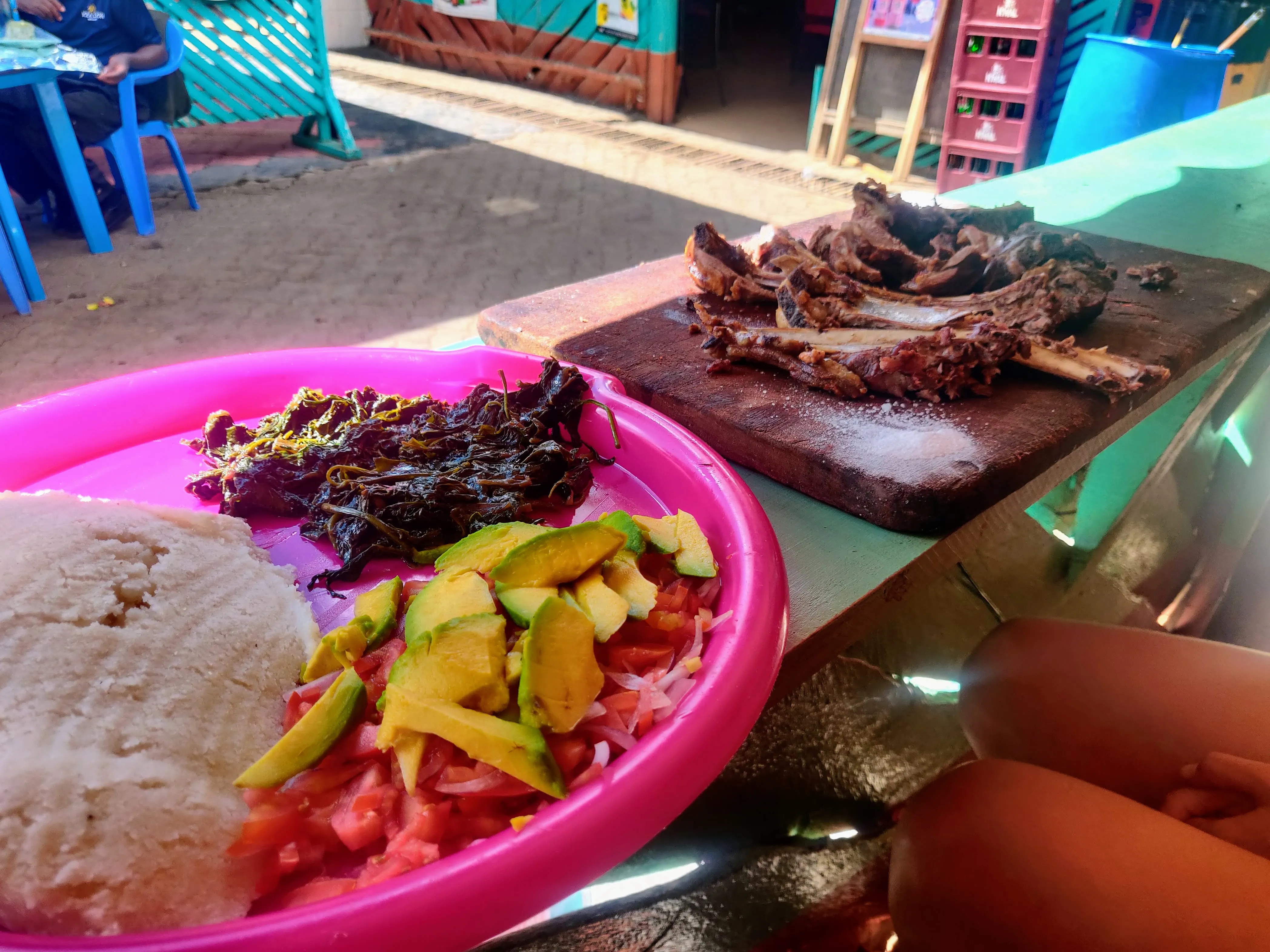 Ugali, nyama choma, sukuma wiki and avocado kachumbari on a pink plate